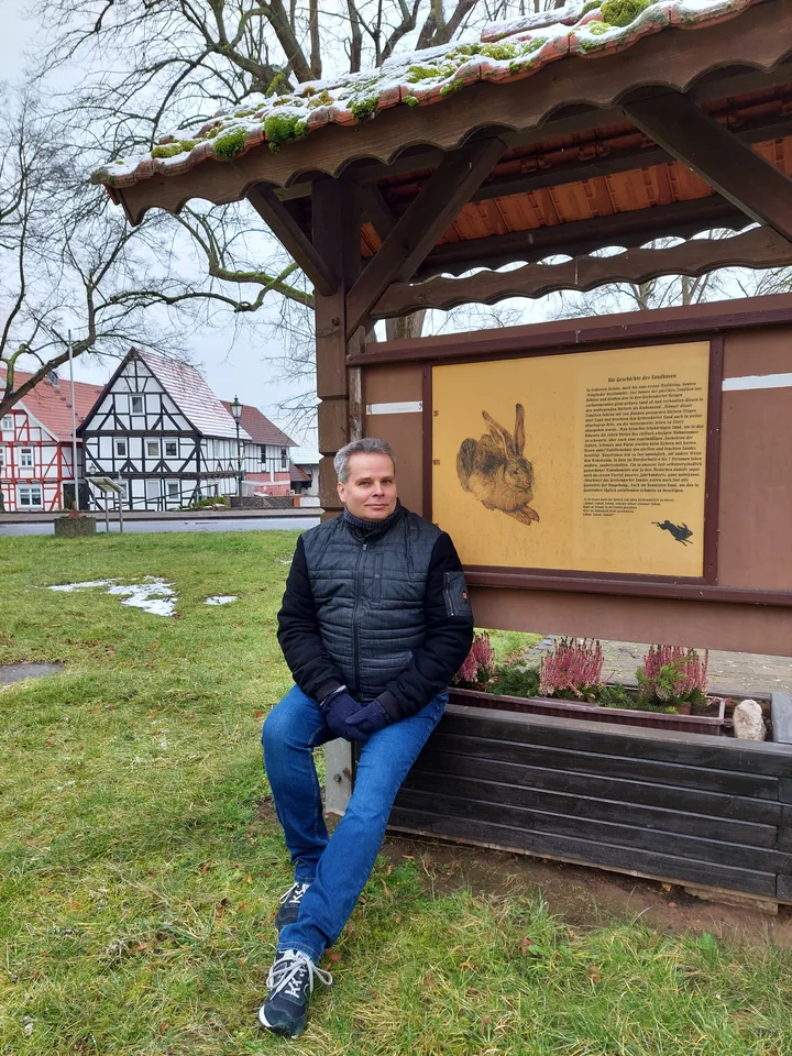 Torsten Schönberg sitzt auf einer Bank an der Sandhasen-Tafel am Anger in Grebendorf.