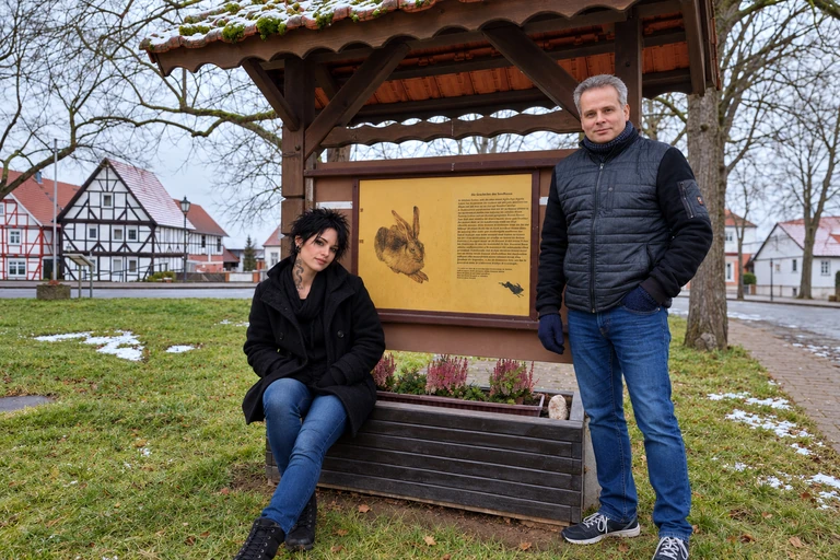 Mascha Sonnenburg sitzt links, Torsten Schönberg steht rechts vor Dieter Schönbergs Hasenbild in Grebendorf.