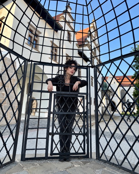 AI photomontage: Mascha stands behind the bars of an iron cage in Levoča, resting her forearms on a crossbar.